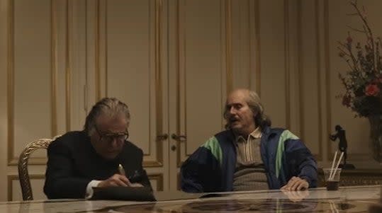 Aldo and Paolo sitting at a table, with the former signing a contract relinquishing his shares of Gucci in "House of Gucci"