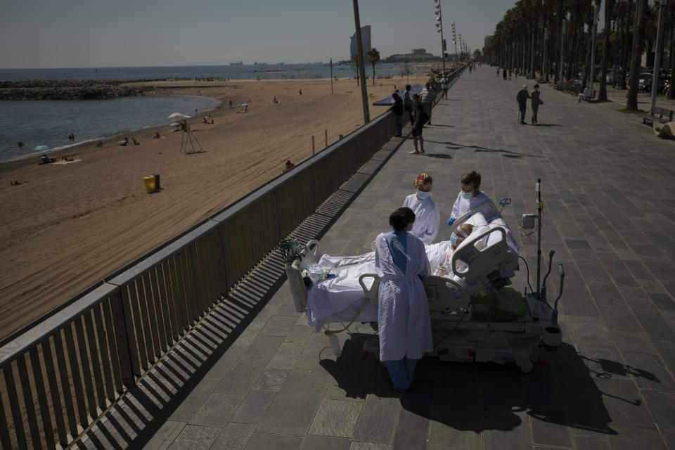 Francisco España, 60, is surrounded by members of his medical team as he looks at the Mediterranean sea from a promenade next to the "Hospital del Mar" in Barcelona, Spain, Friday, Sept. 4, 2020. A hospital in Barcelona is studying how short trips to the beach may help COVID-19 patients recover from long and traumatic intensive hospital care. The study is part of a program to “humanize” ICUs. Since re-starting it in early June, the researchers have anecdotally noticed that even ten minutes in front of the blue sea waters can improve a patient’s emotional attitude. (AP Photo/Emilio Morenatti)