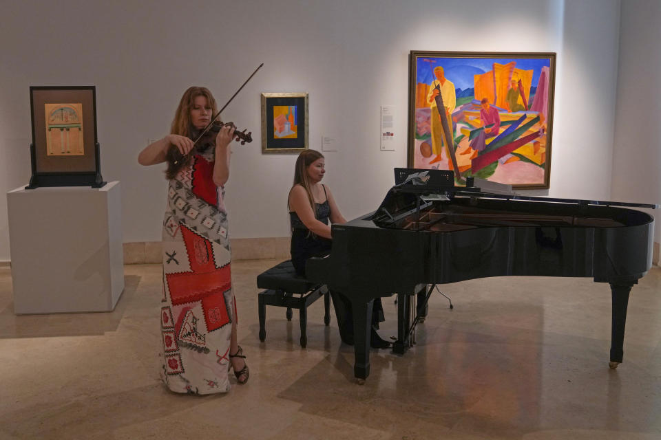 A violinist and a pianist play in front of a painting by Ukrainian artist Oleksandr Bohomazov called 'Sharpening of the Saws', seen at right, during the inauguration of the Ukraine art exposition at the Thyssen-Bornemisza museum in Madrid, Spain, Monday, Nov. 28, 2022. Against a backdrop of Russian attacks, border closures and a nail-biting journey across Europe, Madrid’s Thyssen-Bornemisza National Museum has teamed up with Kyiv’s National Art Museum of Ukraine to secretly bring dozens of Ukrainian 20th century avant-garde artworks to the Spanish capital for a unique exhibition and a show of support for the war-torn country. (AP Photo/Paul White)