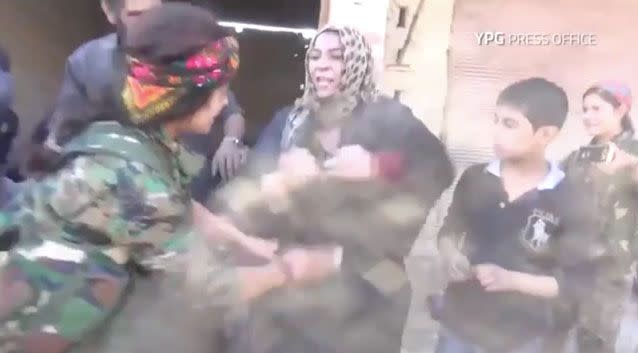 The woman removes her burqa while jumping up and down to reveal a colourful sash underneath. Photo: YPG