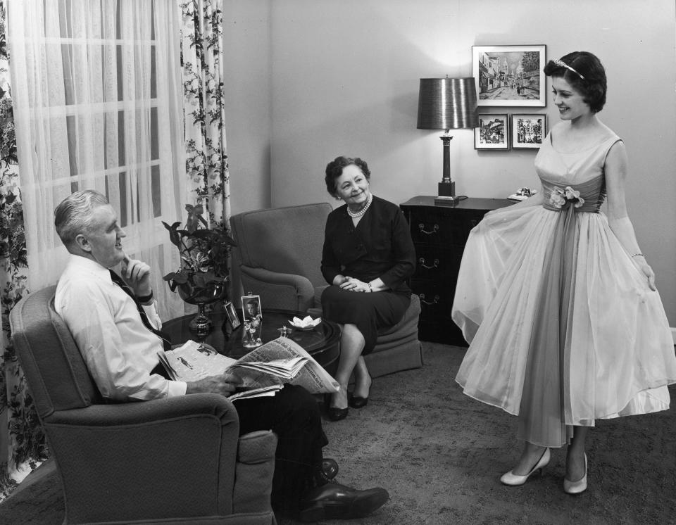 Full-length image of a teenager showing off her prom dress to her parents in their living room, circa 1945