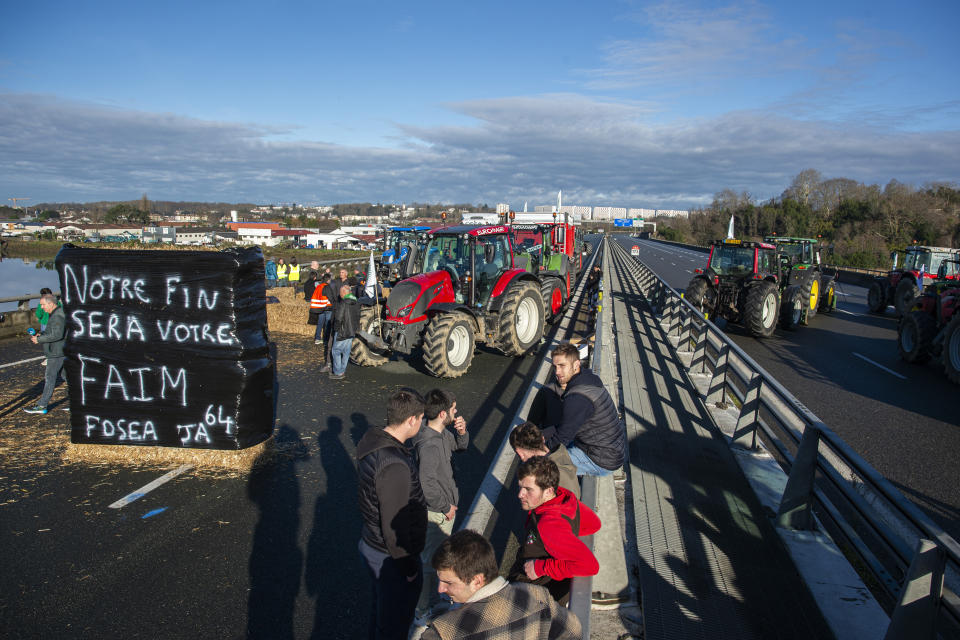 French farmers block the Hubert Touya viaduct on a highway Tuesday, Jan. 23, 2024 in Bayonne, southwestern France. Farmers have for months been protesting for better pay and against what they consider to be excessive regulation, mounting costs and other problems. Banner reads, playing with words: Your end will be our hunger. (AP Photo/Nicolas Mollo)