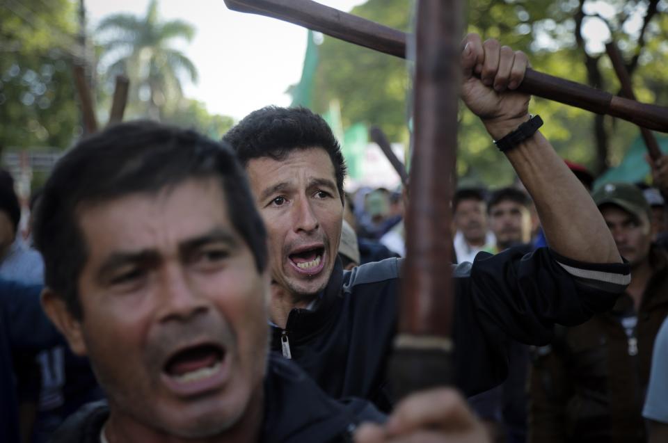 In this Thursday, March 21, 2019 photo, farmers raise wooden clubs and shout slogans against the government of President Mario Abdo Benitez during their National Farmers Federation annual march in Asuncion, Paraguay. They are demanding more land and support from government. (AP Photo/Jorge Saenz)