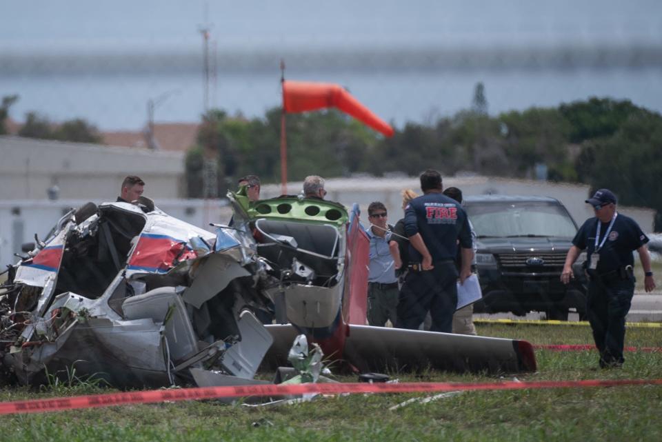 Emergency services personnel stand by a crashed aircraft lying on the ground at Lantana Airport on Friday, May 26, 2023. According to the Palm Beach Sheriff's Office, two passengers aboard were killed in the crash Friday morning.