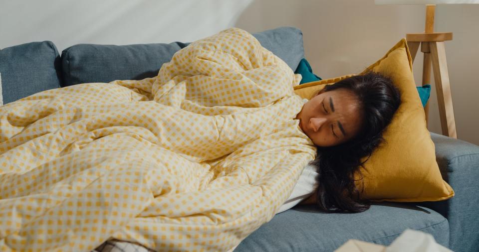 hungover woman under duvet on sofa