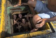 Men pose for a photo from the inside of a cistern of an abandoned building, occupied by squatters, in Rio de Janeiro, Brazil, Wednesday, April 9, 2014. Thousands of people have laid claim to a compound of abandoned office buildings owned by the private telecommunications company Oi, and named their settlement after the state-owned telecommunications Telerj. Authorities are negotiating with squatters to leave peacefully from the area they have occupied for more than a week. (AP Photo/Silvia Izquierdo)