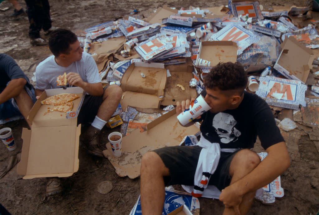 Concert goers at the 25th anniversary concert festival of Woodstock share pizza admits the trash of the event in August of 1994 outside of Saugerties, New York