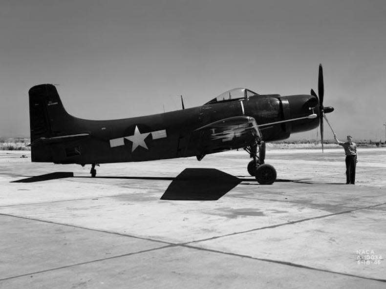 A black and white picture of man posing for a picture with his hand on the propellor of a Douglas XBT2D-1 Skyraider.