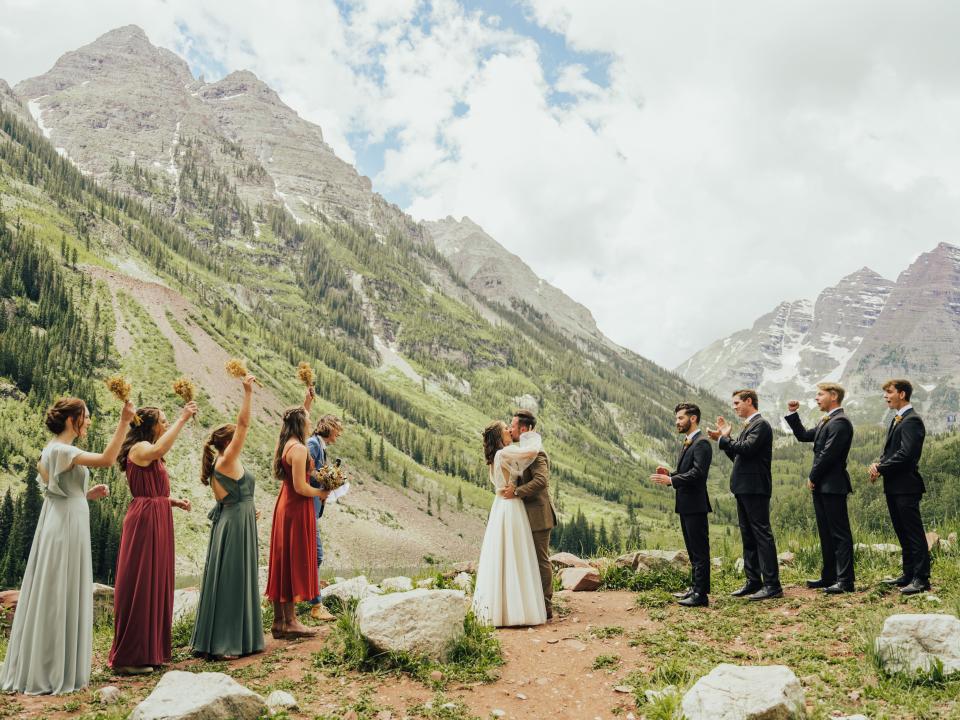 abi and her husband embracing during their wedding ceremony in aspen with their bridal party cheering around them