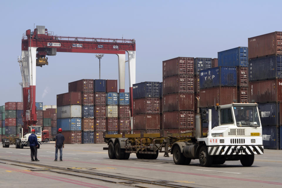 FILE - In this July 24, 2019, file photo, workers watch as a truck passes by stacks of shipping containers at a port in Yingkou in northeastern China's Liaoning Province. Shortages of power, computer chips and other parts, soaring shipping costs and shutdowns of factories to battle the pandemic are taking a toll on Asian economies. (AP Photo/Olivia Zhang, File)