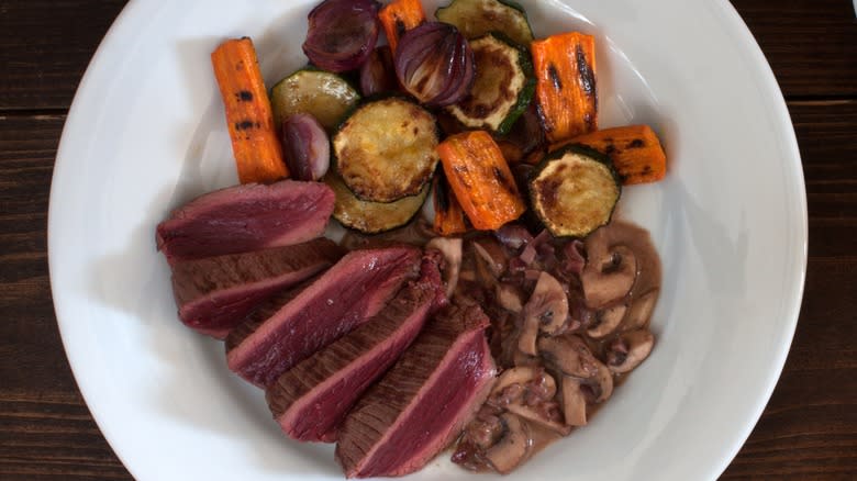 Sliced seared ostrich steak with veggies on a plate
