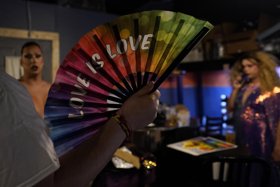 Ryan Geiger holds a rainbow "Love is Love" fan as drag queens Harpy Daniels, aka Joshua Kelley, left, and twin Trixy Valentine, aka Jacob Kelley, right, prepare to perform at Rainbow Special Interest Group of NAFSA: Association of International Educators reception at Pitchers and a League of Her Own bar in Washington, Wednesday, May 31, 2023. (AP Photo/Carolyn Kaster)