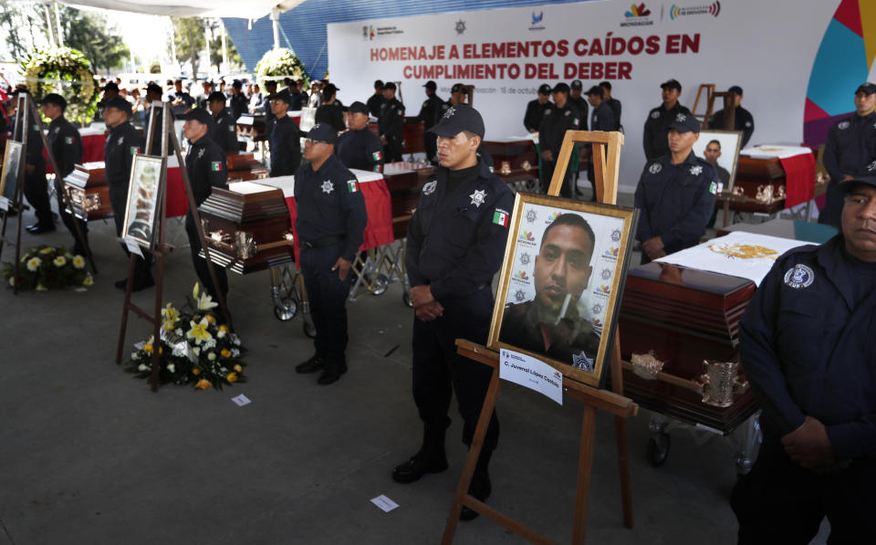 In this Oct. 15, 2019 photo, Michoacan state police stand next to the coffins of slain colleagues during a memorial service at the public security department headquarters for Michoacan state, in Morelia, Mexico. More than 30 suspected cartel gunmen ambushed the police officers in the town of El Aguaje on Monday as they were traveling in a convoy to serve a warrant, killing 13 officers and wounding nine others. (AP Photo/Marco Ugarte)