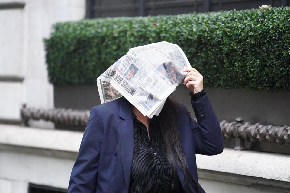 A woman shelters from rain beneath a newspaper (Jordan Pettitt/PA Wire)