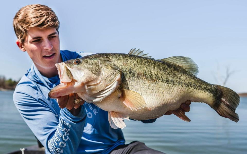 Texas angler Tyler Anderson hefts a giant largemouth bass with lake in background