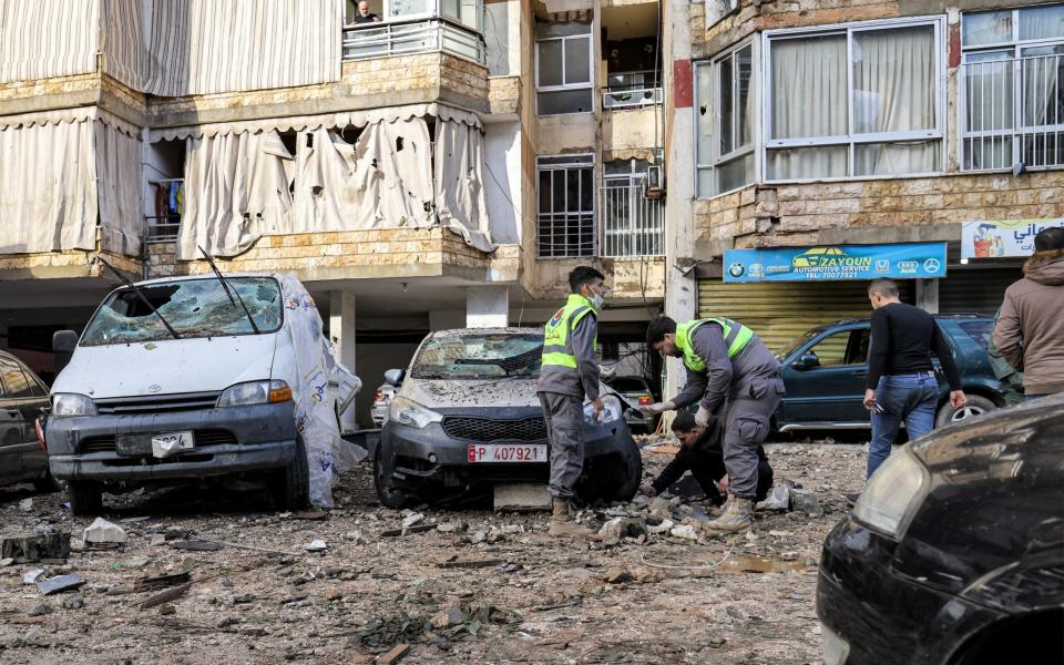 Civil defence workers inspect a vehicle that was damaged near the building hit by a suspected Israeli strike