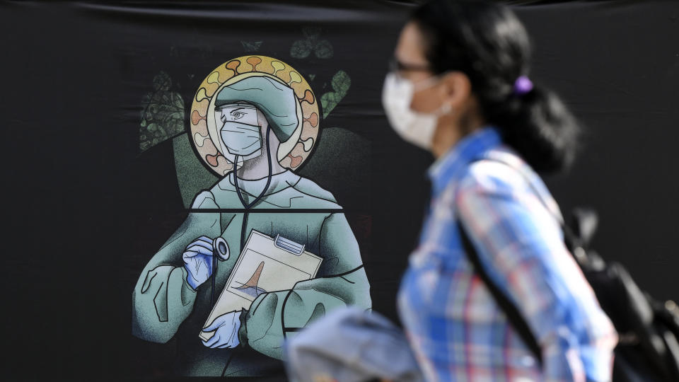 A woman walks by a depiction of a medical staff wearing protective equipment, executed in the style of orthodox icons, in Bucharest, Romania, Wednesday, April 29, 2020. The artwork, among others depicting medical staff in the manner of religious icons, created by designer Wanda Hutira, is part of a campaign called Thank You Doctors, meant to raise awareness to the work of medical staff fighting the COVID-19 pandemic. Following public pressure by Romania's influential Orthodox church the artworks, described as "blasphemous" will be removed from all locations in the Romanian capital, according to the agency behind the project. (AP Photo/Andreea Alexandru)