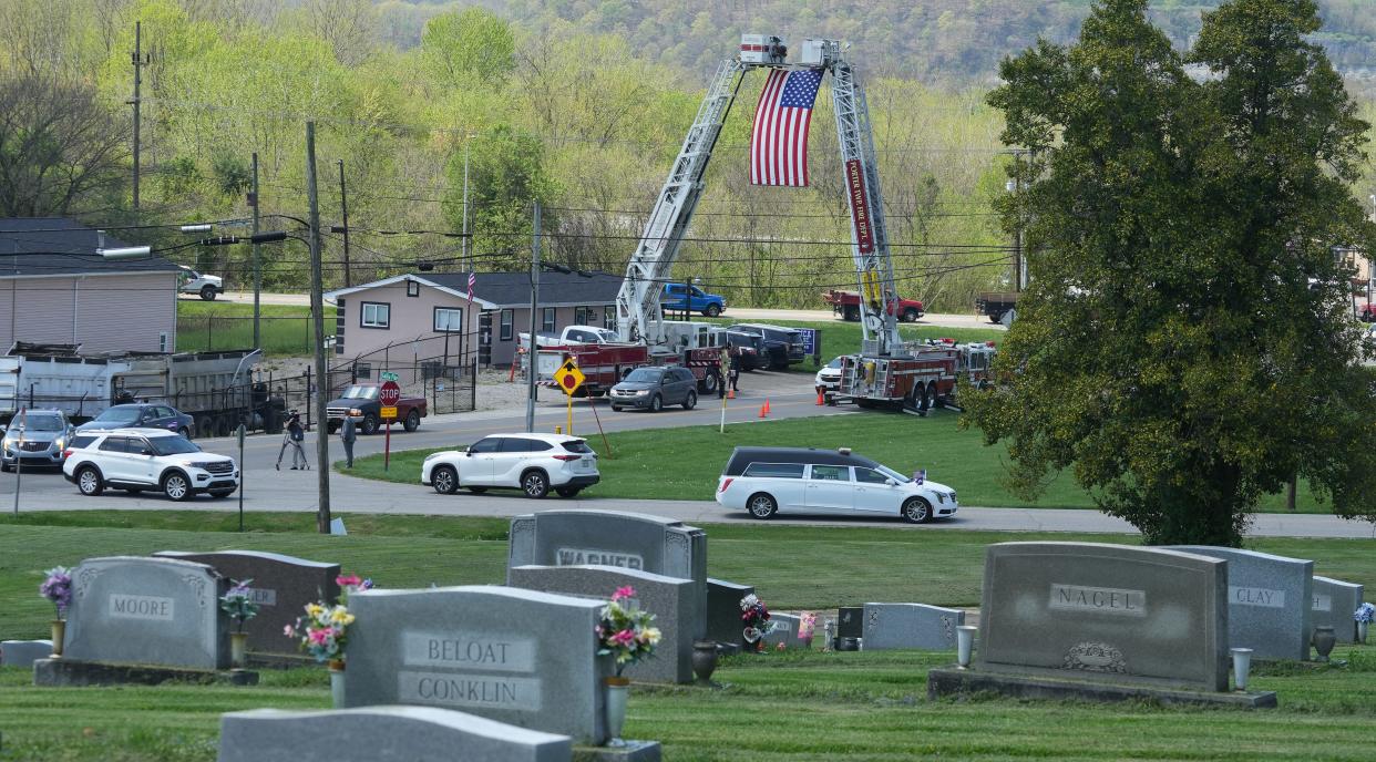 Under flag-draped ladder fire trucks, the funeral procession of Lt. Rodney Osborne arrives Monday at Memorial Burial Park in Wheelersburg, Scioto River. Osborne was fatally shot in the chest on April 9 at the firing range at the Ohio Department of Rehabilitation and Correction's prison training facility in Orient, Pickaway County. More than a hundred cars were in the funeral procession.