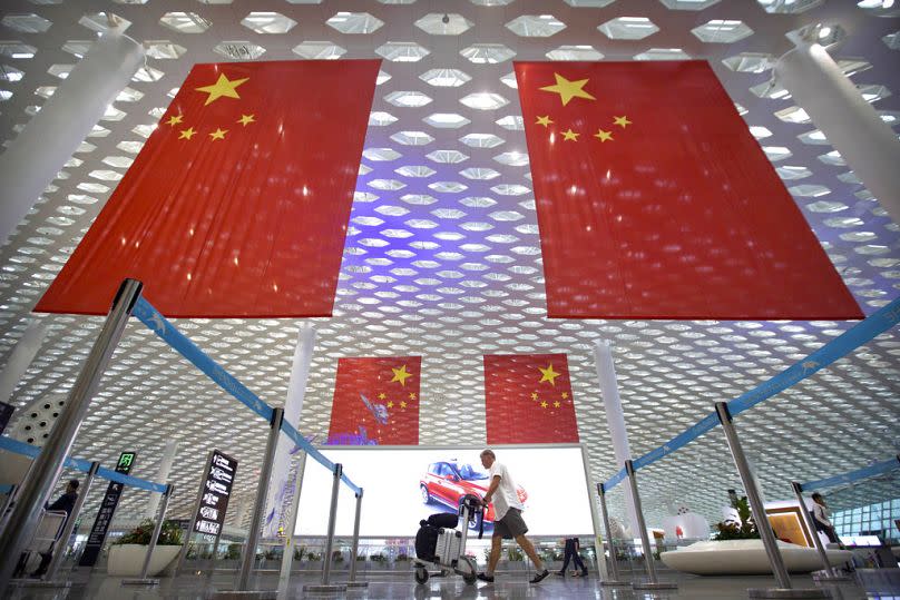 A traveler pushes his luggage beneath large Chinese flags on hanging from the ceiling in Shenzhen Bao'an International Airport in Shenzhen, October 2018