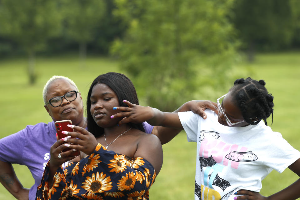 Zakia Buchanan, center, shows TikTok videos to her mom, Delicia Harris, left, as her youngest sister Antoinette Harris, touches her face Thursday, July 22, 2021 at Rock Cut State Park in Loves Park, Ill. The eruption in violence in the city among people stuck at home wasn't a surprise to Harris who has worked with youth programs in Rockford. The money flowing to cities and states from the American Rescue Plan is so substantial and can be used for so many purposes that communities across the U.S. are trying out new, longer-term ways to fix what’s broken in their cities. (AP Photo/Shafkat Anowar)
