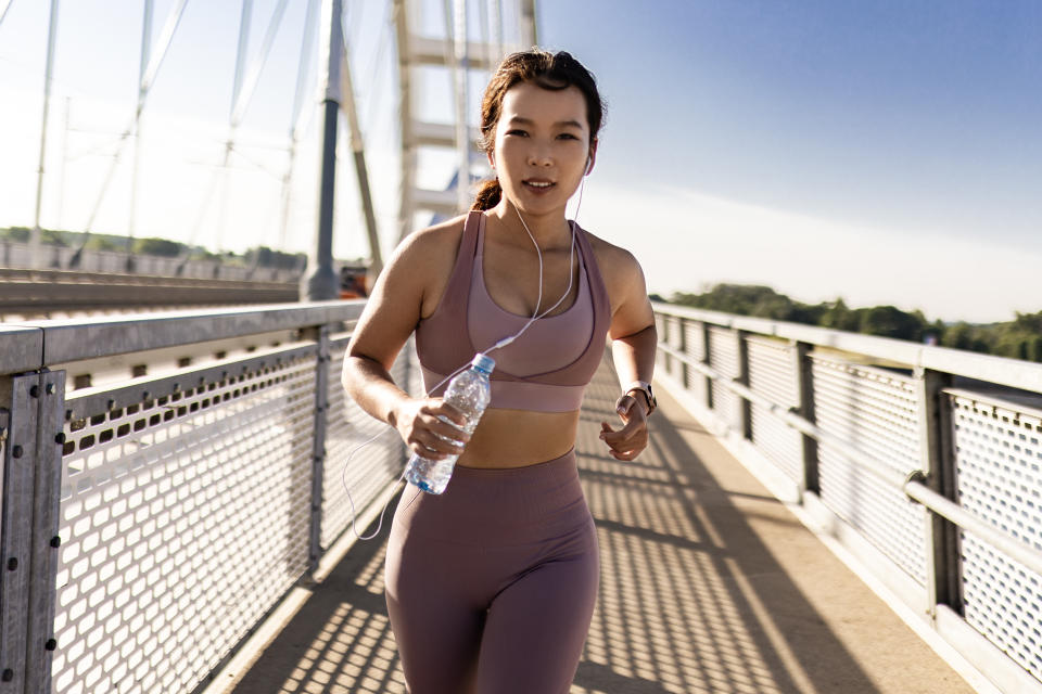 Cheerful Asian female runner jogging on city bridge
