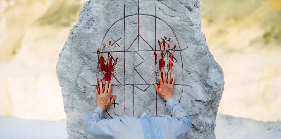 Person puts bloody hands against stone.