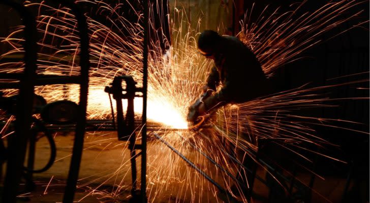 Person working on metal in the dark, with sparks flying. industrial stocks