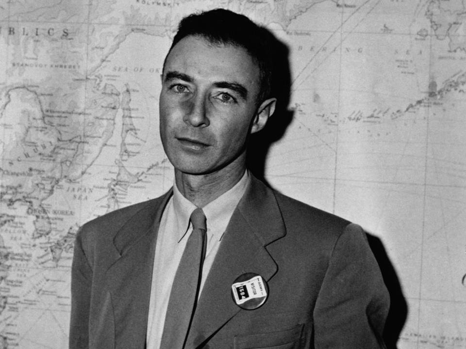 J. Robert Oppenheimer poses for a photograph in front of a map.