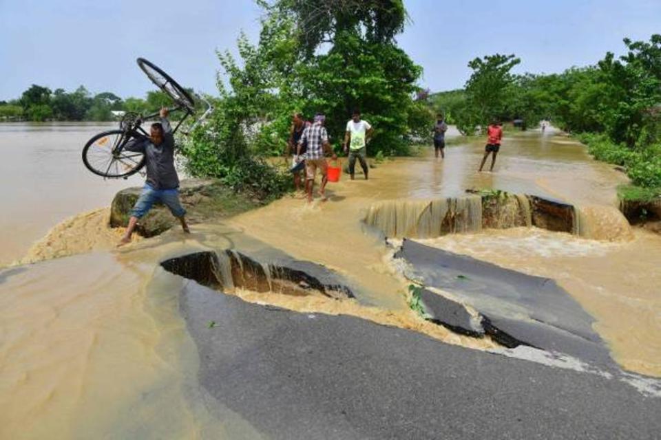 A man carrying his bicycle wades along a road partially damaged due to flooding in Nagaon district on 19 May (AFP via Getty)