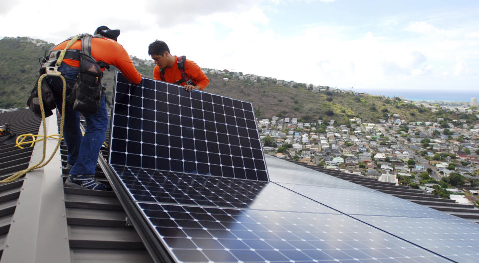 FILE - In this July 8, 2016, file photo, Radford Takashima, left, installer for RevoluSun, and lead installer Dane Hew Len, right, place solar panels on a roof in Honolulu. If you have the cash, most experts agree buying a solar system outright is a better investment than leasing or taking out a loan. Customers should check electric bills to estimate monthly energy use when deciding what size system to buy, and calculate federal or state incentives. (AP Photo/Cathy Bussewitz, File)