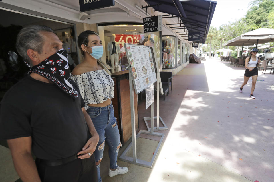 Restaurant workers Alvyn Lopez, left, and Maria Lindo watch for customers as they stand outside Aura at Books & Books, Monday, July 6, 2020, on Miami Beach, Florida's famed Lincoln Road. In Miami-Dade County, population 2.7 million, Mayor Carlos Gimenez ordered the closing of restaurants and certain other indoor places, including vacation rentals, seven weeks after they were allowed to reopen. Beaches will reopen on Tuesday after being closed over the weekend. (AP Photo/Wilfredo Lee)