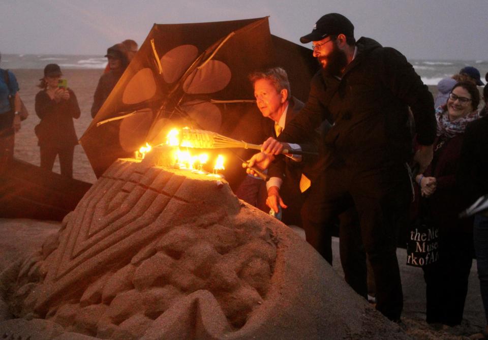 Palm Beach County Commissioner Gregg Weiss (left) and Rabbi Leib Ezagui huddle together in the rain to light nine candles on a sand-sculpture menorah that crews rebuilt after vandals destroyed it on Monday in Juno Beach.