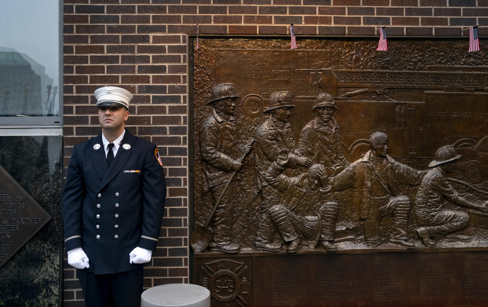 A New York City firefighter stands at attention in front of a memorial on the side of a firehouse adjacent to One World Trade Center and the 9/11 Memorial site during ceremonies on the anniversary of 9/11 terrorist attacks in New York on Tuesday, Sept. 11, 2018. (AP Photo/Craig Ruttle)