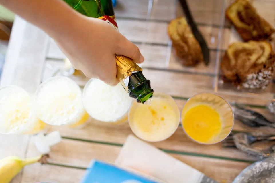 Pouring Champagne into orange juice glasses.