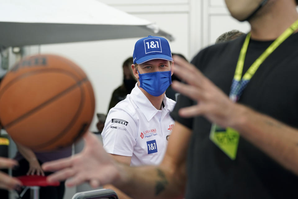 Haas driver Mick Schumacher of Germany, left, works with former NBA player Fabricio Oberto, right, at the Formula One U.S. Grand Prix auto race at the Circuit of the Americas, Thursday, Oct. 21, 2021, in Austin, Texas, as he practices before F1 Teams take part in a free throw challenge as they help the NBA celebrate their 75th Anniversary. (AP Photo/Eric Gay)