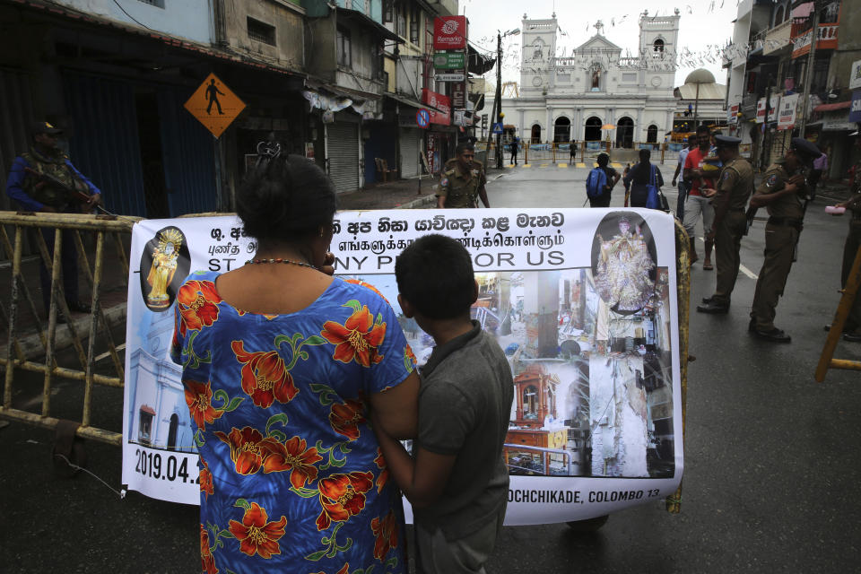 A Sri Lankan mother and son look at poster outside St. Anthony's Church in Colombo, Sri Lanka, Tuesday, April 30, 2019. Sri Lanka is limping back to normalcy after the devastating bomb attacks on Easter Sunday that killed more than 250 people, meanwhile the archbishop said that the government's security operations to apprehend Islamic extremists who may be at large is unsatisfactory despite assurances from leaders. (AP Photo/Manish Swarup)