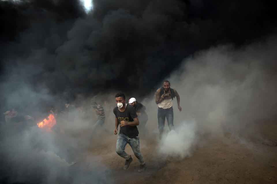 Palestinians run for cover from teargas fired from Israeli troops during a protest at the Gaza Strip's border with Israel, Friday, Oct. 5, 2018. (AP Photo/Khalil Hamra)