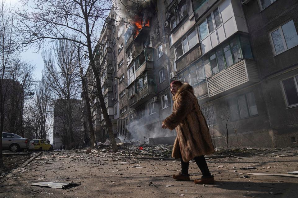 A woman walks past a burning apartment building after shelling in Mariupol, Ukraine, on March 13, 2022.