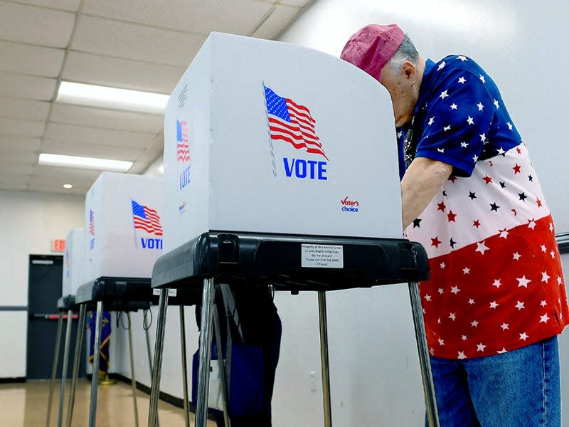 Man in a red, white, and blue shirt voting in a voting center for 2022 midterm elections.