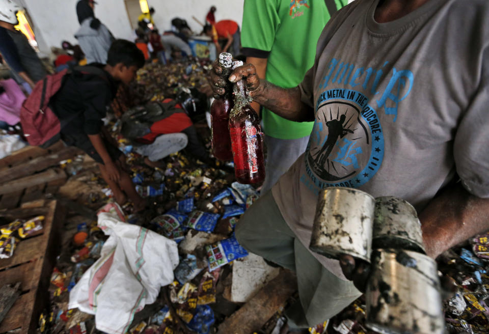 A man holds bottles of syrup and cans of condensed milk scavenged from an abandoned warehouse at an earthquake and tsunami-affected area in Palu, Central Sulawesi, Indonesia Indonesia, Wednesday, Oct. 3, 2018. Clambering over the reeking pile of sodden food or staking out a patch of territory, people who had come from devastated neighborhoods and elsewhere in the remote Indonesian city pulled out small cartons of milk, soft drinks, rice, candy and painkillers from the pile as they scavenge for anything edible in the warehouse that tsunami waves had pounded. (AP Photo/Dita Alangkara)