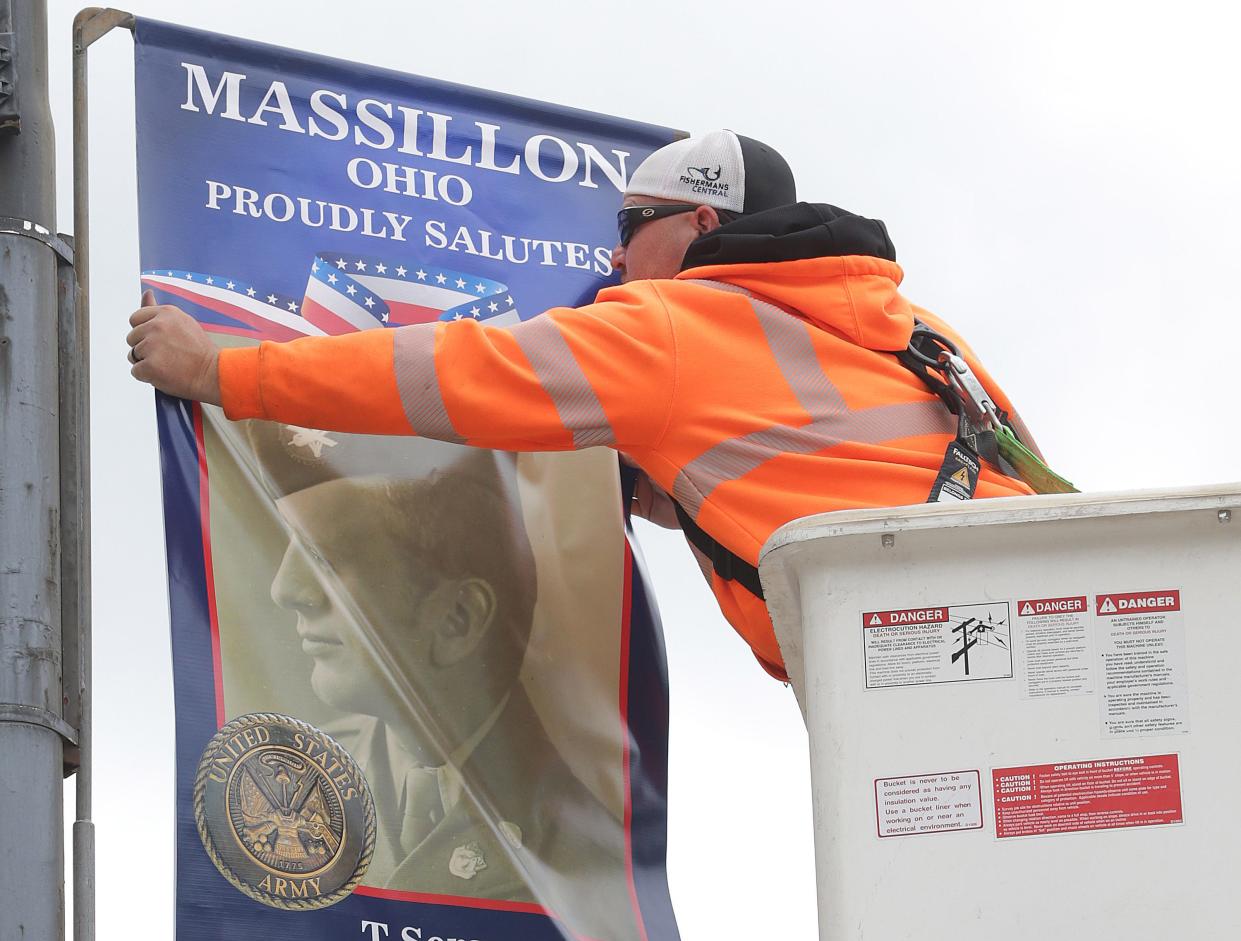 Massillon Safety Department employee Scott Pettry hangs a banner of one of Massillon's deceased veterans along Lincoln Way in downtown Massillon. Fifteen banners featuring 29 veterans will be on display. Additional banners with active military members and living veterans will be added next month as part of a program to honor service members from western Stark County.