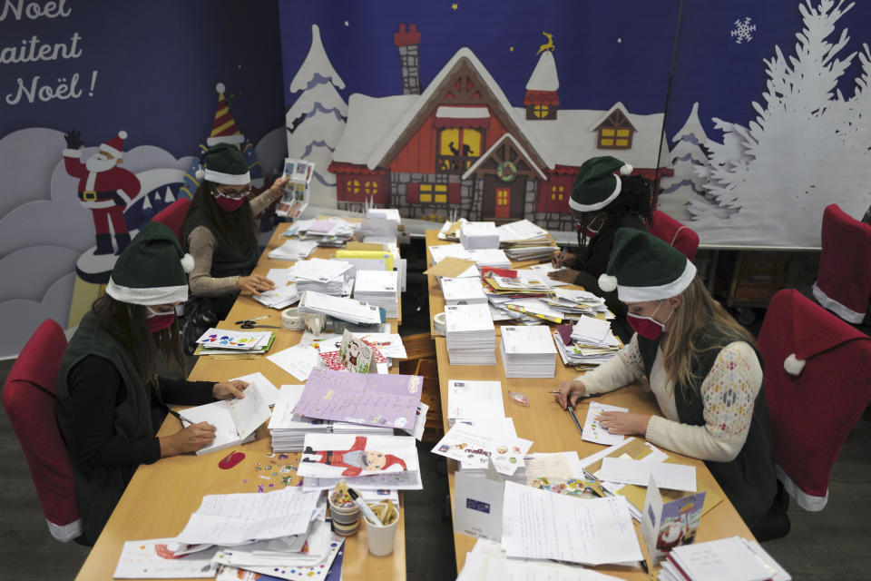 Postal workers who call themselves "Elves" open envelopes addressed to "Pere Noel" - Father Christmas in French - decorated with love hearts, stickers and glitter, in Libourne, southwest France, Monday, Nov. 23, 2020. Letters pouring by the tens of thousands into Santa's mailbox offer a glimpse into the worries and hopes of children awaiting a pandemic-hit Christmas. Along with usual pleas for toys and gadgets, kids are also mailing requests for vaccines, for visits from grandparents, for life to return to the way it was. The office estimates that one letter in three mentions the pandemic. (AP Photo/Francois Mori)