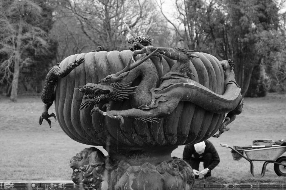 A black and white photo of a large sculpture featuring dragons twisting around a central water bowl.