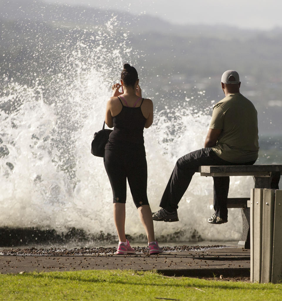 FILE - In this Aug. 31, 2015 file photo, T.J. and Misti Madden, of Hilo, Hawaii, watch as a large wave crashes off a sea wall in Hilo, Hawaii as hurricane Ignacio moves past the state. Some of Hawaii's most iconic beaches could soon be underwater as rising sea levels caused by global warming overtake its white sand beaches and bustling city streets. That’s alarming for a state where beach tourism is the primary economic driver. (AP Photo/Caleb Jones, File)