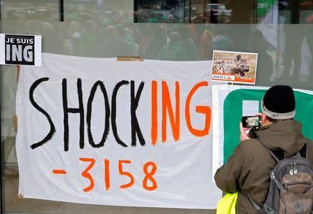 A demonstrator takes a picture near a banner displaying the planned number of job cuts at ING in front of the bank's main office in Brussels, Belgium, October 7, 2016. REUTERS/Francois Lenoir