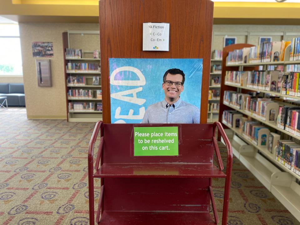 A John Green poster hangs in the teen section of the Hamilton East Public Library on Wednesday, Aug. 9, 2023. But the library has moved copies of one of his most prominent YA novels, "The Fault in Our Stars," to the general collection.