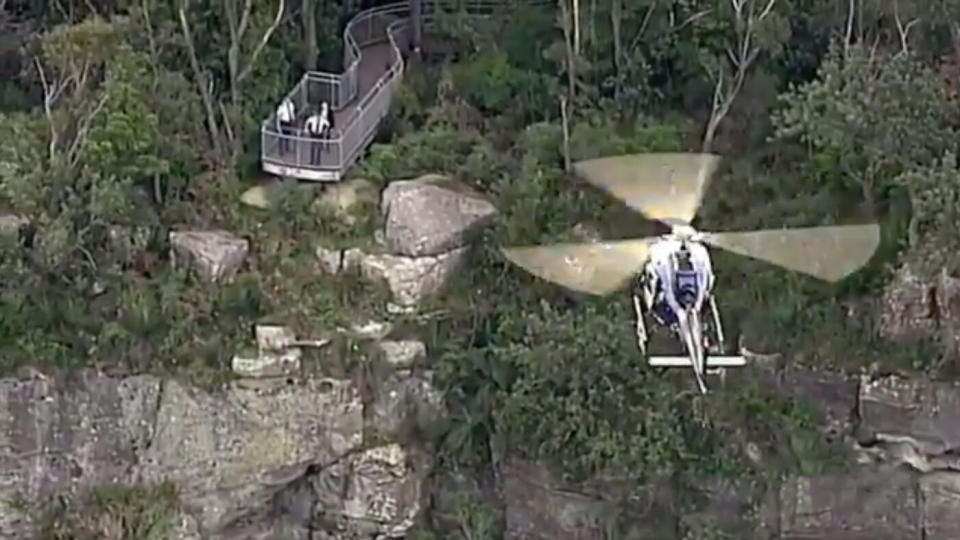 The cliff edge where the mum and her toddler died at Mt Keira is seen on Tuesday. Police stand at the lookout while a helicopter flies over.