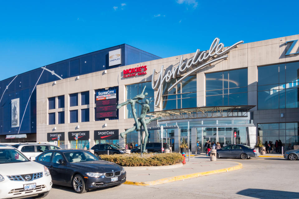 Toronto, Canada - April 5, 2014:  People enter and exit the Yorkdale Shopping Centre with parked cars in the foreground. The mall is one of the largest in Toronto and celebrates its 50th year anniversary in 2014.