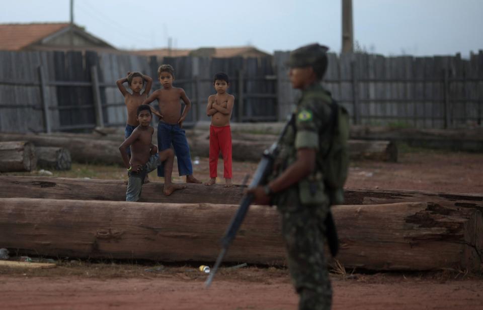 File photo of children observing as a Brazilian Army soldier guards a yard filled with trees illegally extracted from the Amazon jungle in Nova Esperanca do Piria