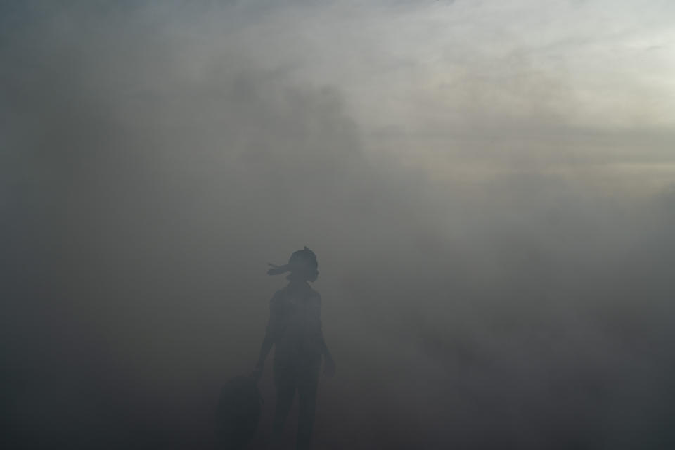 A woman working on a fish processing site walks through the thick smoke coming from burning peanut shells used to cure fish on Bargny beach, some 35 kilometers (22 miles) east of Dakar, Senegal, Wednesday April 21, 2021. In Bargny and other coastal villages of Senegal, traditional fishing and processing of the catch is a livelihood and a pride. Methods have been passed down through generations. Women work as processors — drying, smoking, salting and fermenting the catch brought home by men. (AP Photo/Leo Correa)